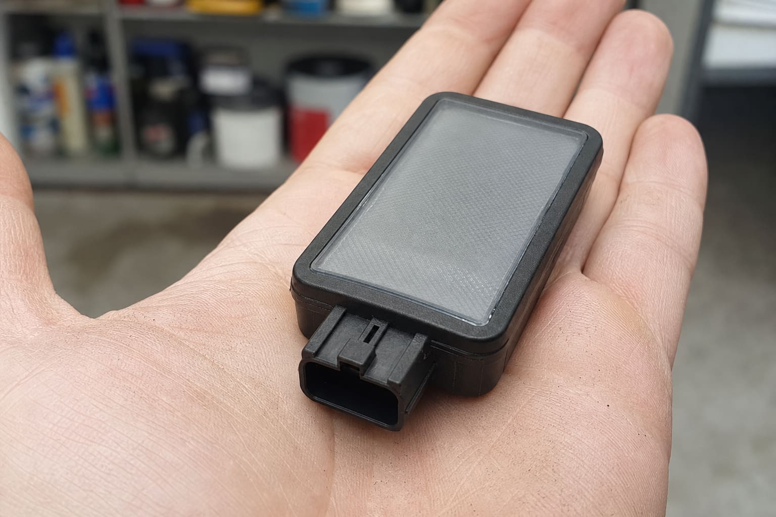 Rectangular OEM rain and light sensor module resting on an open palm, showing the frosted optical coupling window and a keyed automotive connector on one edge